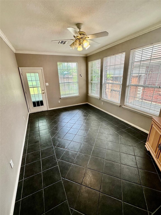 spare room with crown molding, dark tile patterned floors, a ceiling fan, baseboards, and a textured ceiling
