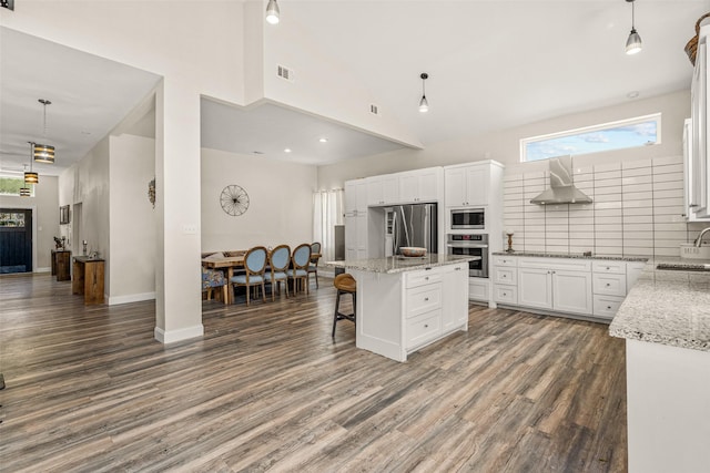 kitchen with hanging light fixtures, a center island, stainless steel appliances, and wall chimney range hood