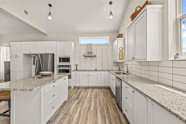 kitchen with wall chimney exhaust hood, decorative light fixtures, appliances with stainless steel finishes, and lofted ceiling with skylight