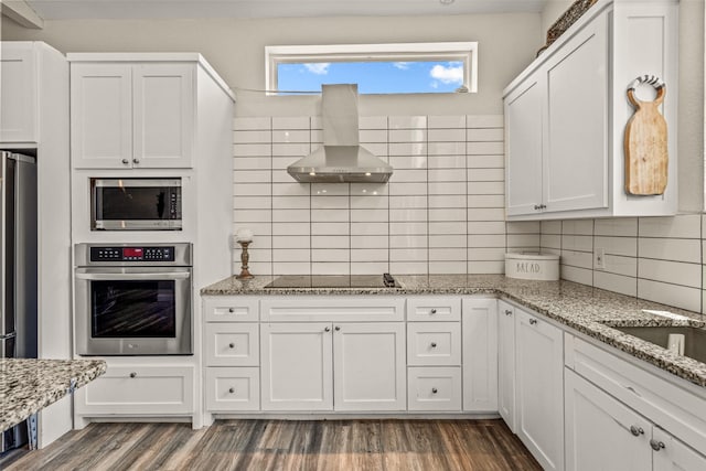 kitchen featuring light stone countertops, stainless steel appliances, range hood, backsplash, and white cabinets