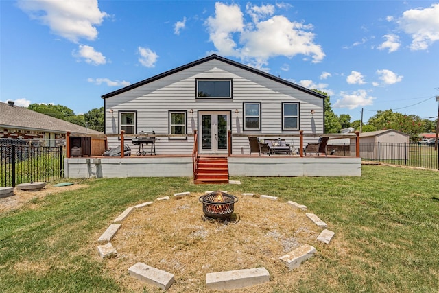 back of property with french doors, a fire pit, a wooden deck, and a lawn