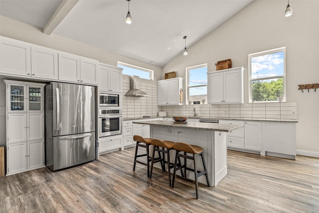 kitchen with a center island, stainless steel appliances, hanging light fixtures, and wall chimney range hood