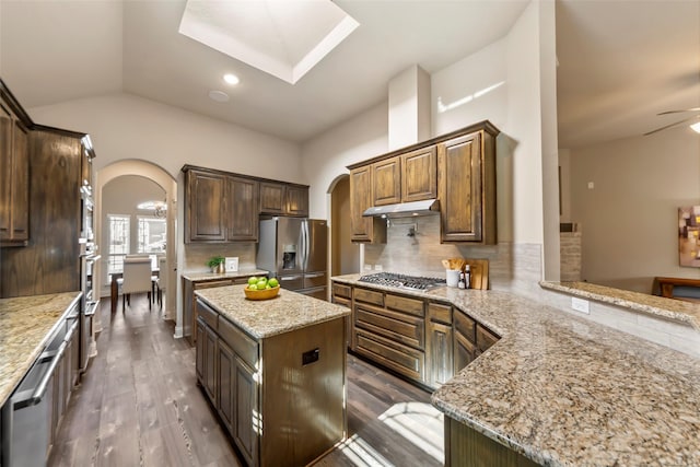 kitchen with stainless steel appliances, light stone countertops, tasteful backsplash, and a center island