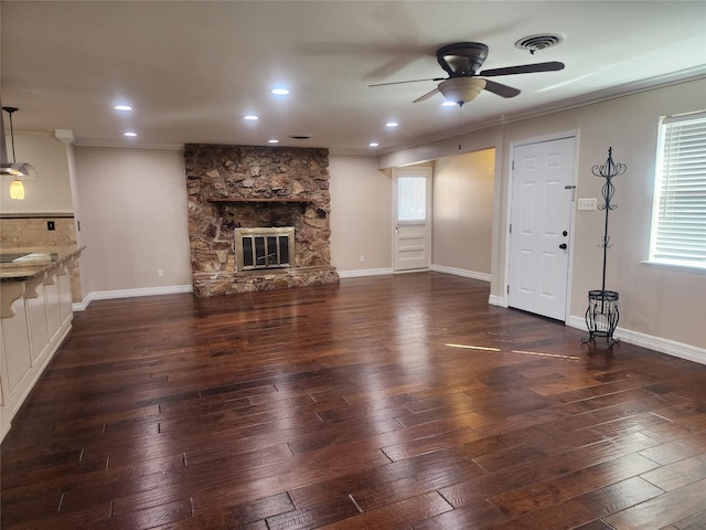 unfurnished living room featuring dark hardwood / wood-style flooring, ceiling fan, ornamental molding, and a stone fireplace