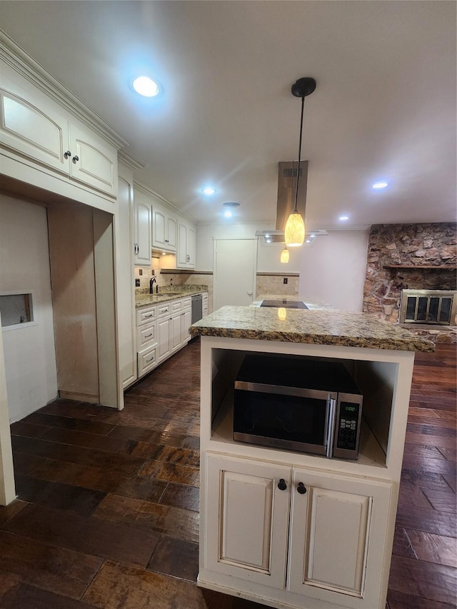 kitchen with light stone counters, island range hood, decorative light fixtures, white cabinetry, and sink