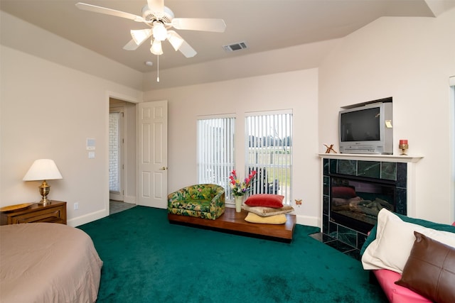 bedroom featuring a tile fireplace, dark carpet, and ceiling fan