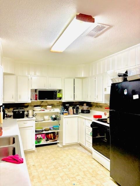 kitchen featuring black refrigerator, sink, a textured ceiling, gas range gas stove, and white cabinetry