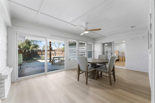 dining room with a ceiling fan, light wood finished floors, brick wall, and visible vents
