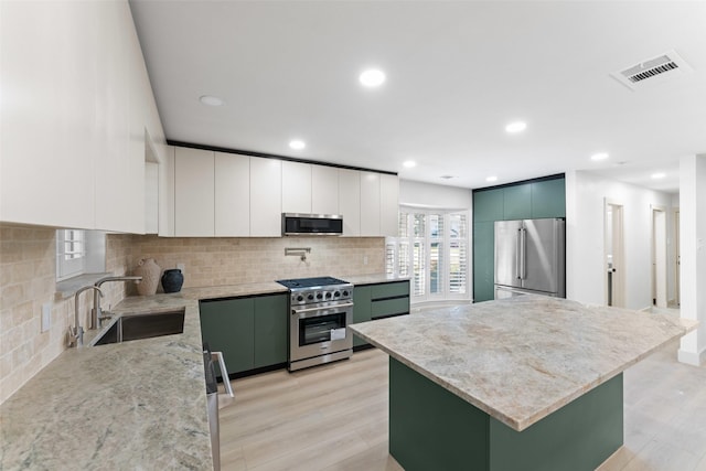 kitchen featuring visible vents, high end appliances, a sink, light wood-style floors, and green cabinetry