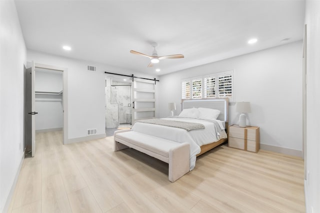 bedroom featuring visible vents, a barn door, and light wood-style flooring