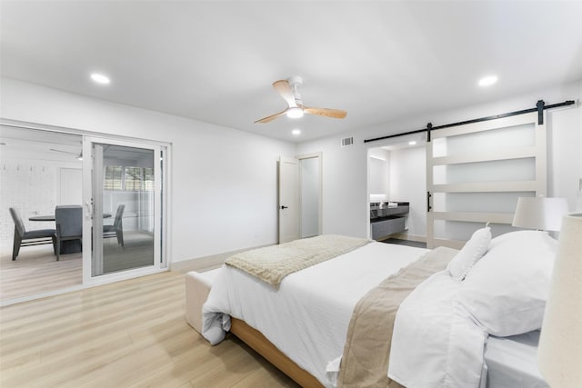 bedroom with visible vents, a barn door, light wood finished floors, and recessed lighting