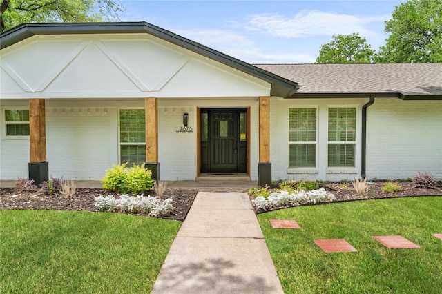 property entrance with a lawn, covered porch, a shingled roof, and brick siding