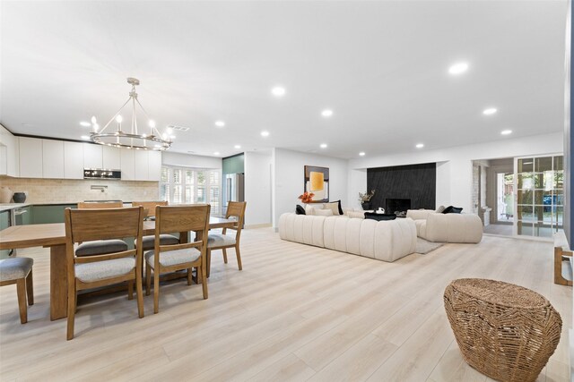 living room featuring recessed lighting, a fireplace, light wood finished floors, and a chandelier