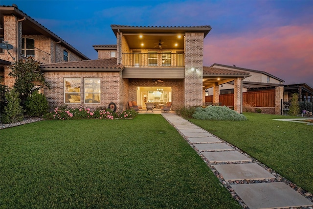 view of front of property featuring a lawn, ceiling fan, a balcony, and a patio