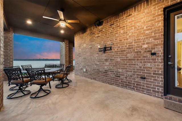 patio terrace at dusk featuring a water view and ceiling fan