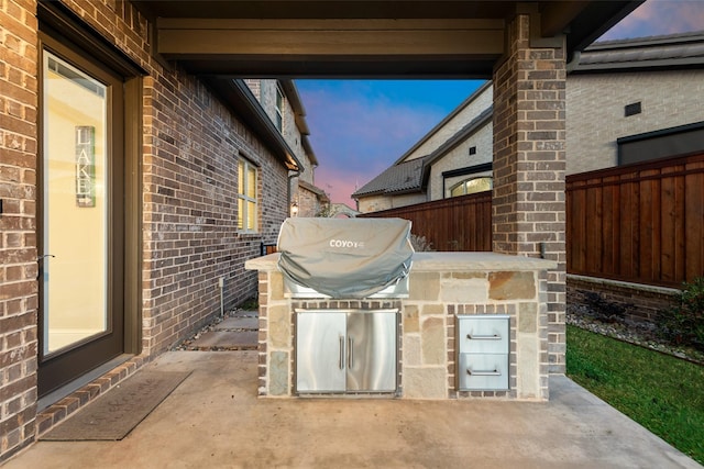 patio terrace at dusk featuring an outdoor kitchen and area for grilling