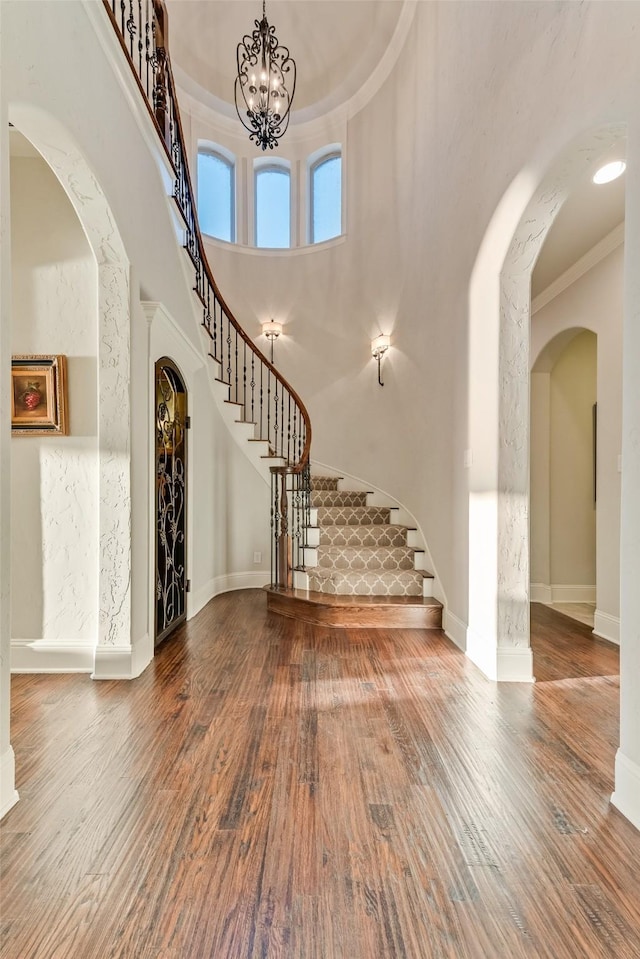 entrance foyer with hardwood / wood-style floors, a towering ceiling, crown molding, and a notable chandelier