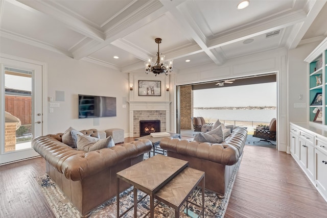 living room featuring beam ceiling, coffered ceiling, a stone fireplace, ornamental molding, and hardwood / wood-style flooring