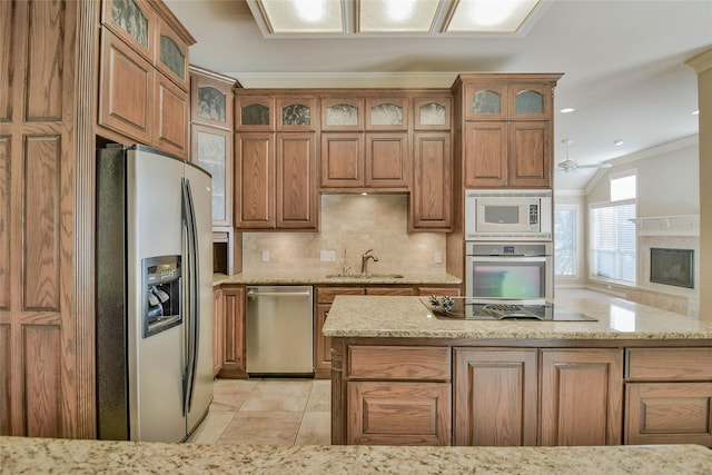 kitchen with light stone counters, stainless steel appliances, ceiling fan, crown molding, and sink