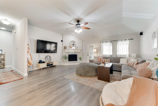 living room featuring ceiling fan, a large fireplace, light wood-type flooring, and lofted ceiling