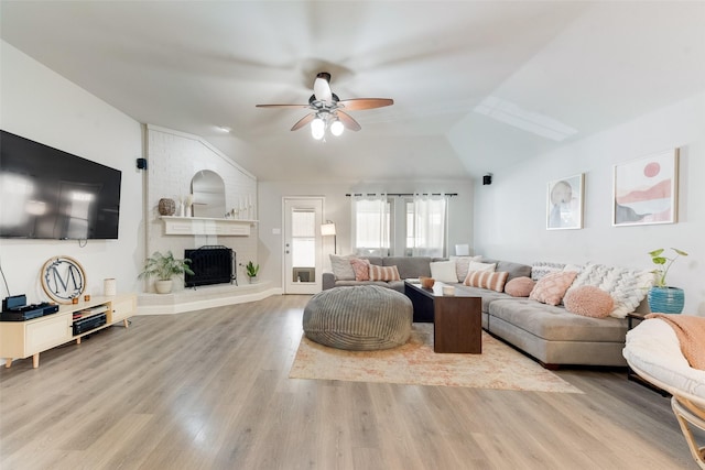 living room featuring ceiling fan, light wood-type flooring, a fireplace, and vaulted ceiling