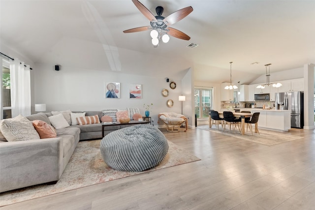 living room with ceiling fan with notable chandelier, light wood-type flooring, and lofted ceiling