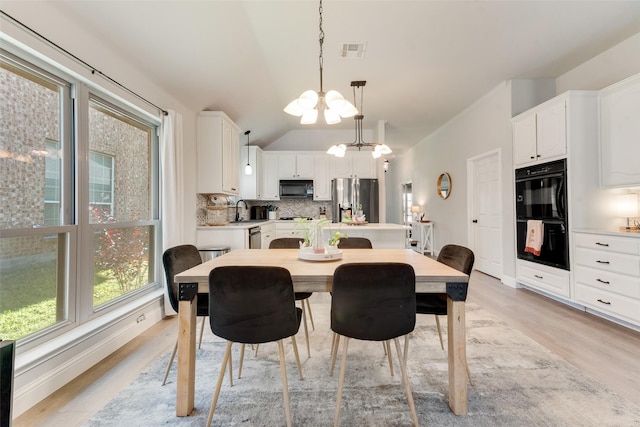 dining room featuring light hardwood / wood-style flooring, an inviting chandelier, lofted ceiling, and sink