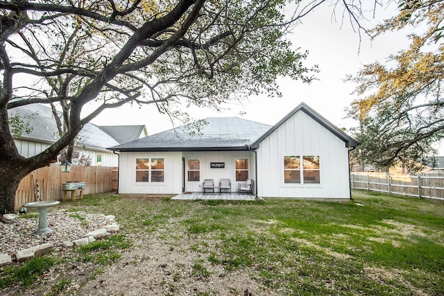 rear view of house with a patio, a fenced backyard, roof with shingles, a yard, and board and batten siding