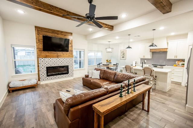 living room featuring light hardwood / wood-style floors, ceiling fan, a tile fireplace, and beamed ceiling