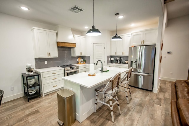 kitchen with a breakfast bar, premium range hood, appliances with stainless steel finishes, white cabinets, and decorative light fixtures