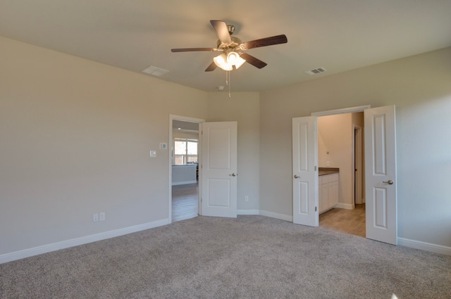 unfurnished bedroom featuring ceiling fan, ensuite bathroom, and light colored carpet