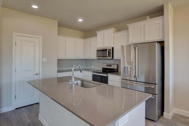 kitchen with an island with sink, stainless steel appliances, white cabinetry, and sink