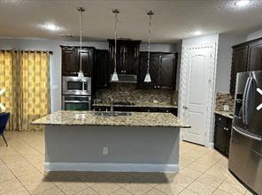 kitchen with sink, stainless steel appliances, tasteful backsplash, pendant lighting, and a center island with sink