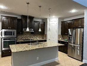 kitchen featuring backsplash, light stone counters, stainless steel appliances, sink, and a center island with sink