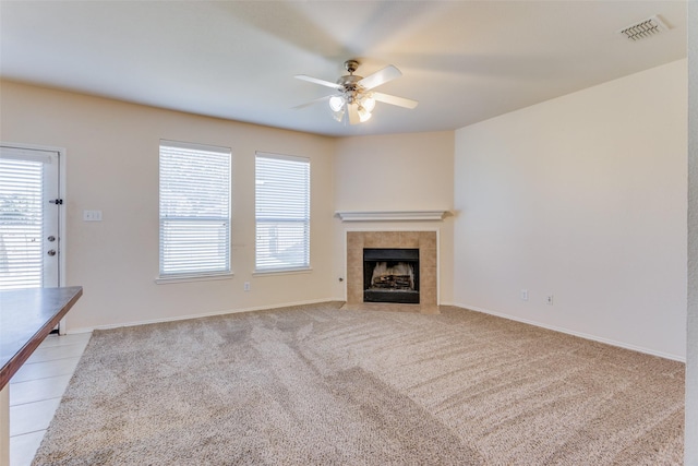 unfurnished living room with a tile fireplace, light colored carpet, and ceiling fan