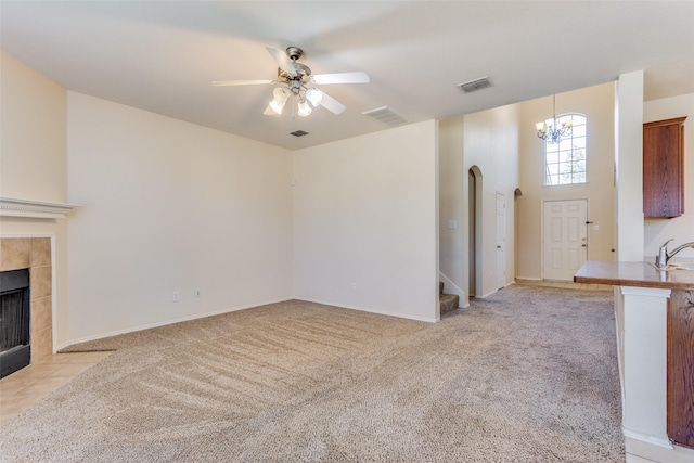 unfurnished living room featuring light carpet, ceiling fan with notable chandelier, sink, and a tiled fireplace