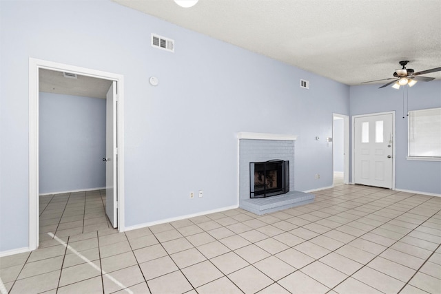 unfurnished living room with ceiling fan, light tile patterned flooring, a textured ceiling, and a brick fireplace