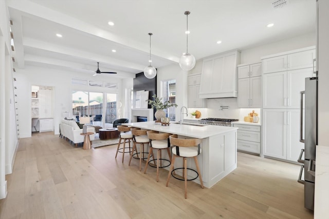 kitchen featuring custom exhaust hood, a kitchen island with sink, white cabinets, hanging light fixtures, and ceiling fan