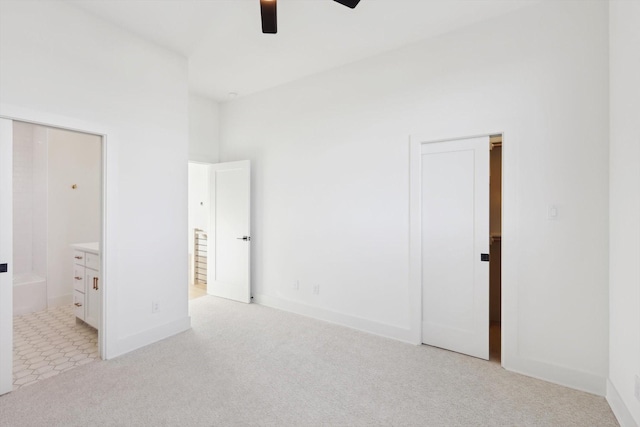 unfurnished bedroom with ensuite bathroom, ceiling fan, light colored carpet, and a high ceiling