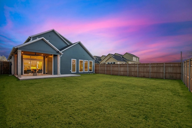 back house at dusk featuring ceiling fan, a yard, and a patio