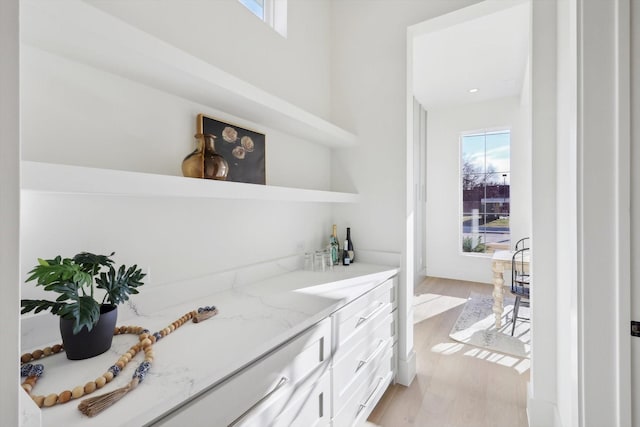 bar with light stone counters, light hardwood / wood-style flooring, and white cabinets