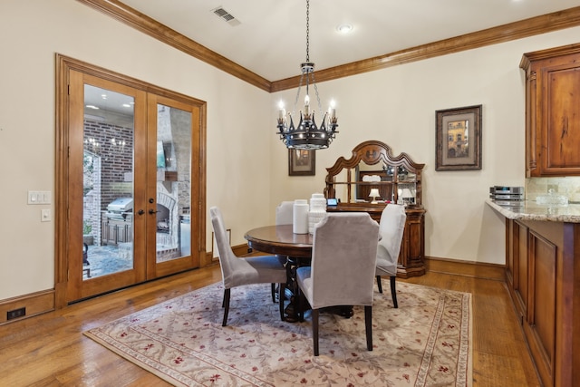 dining room with a chandelier, french doors, light hardwood / wood-style floors, and crown molding