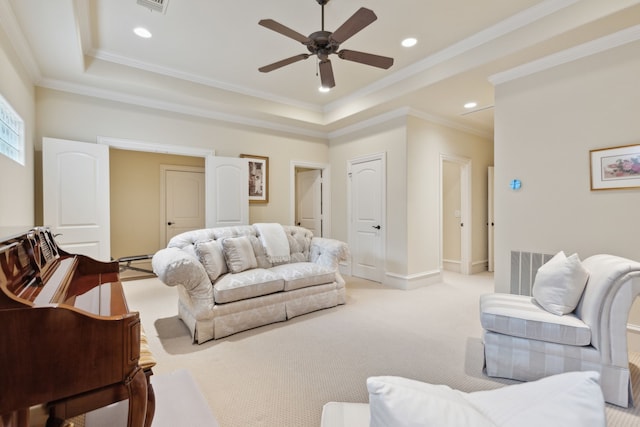 carpeted living room with a raised ceiling, ceiling fan, and crown molding