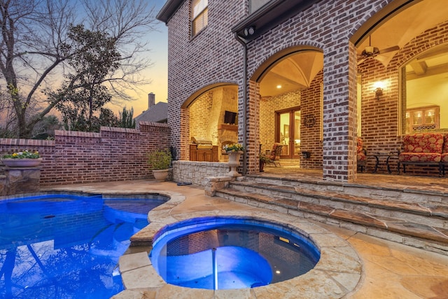 pool at dusk with a patio area and an in ground hot tub