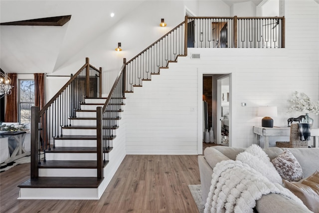 stairs with an inviting chandelier, wood-type flooring, and a high ceiling