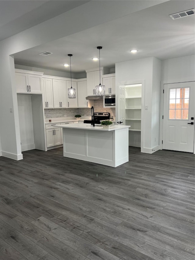 kitchen with a kitchen island with sink, dark wood-type flooring, built in microwave, decorative light fixtures, and white cabinetry