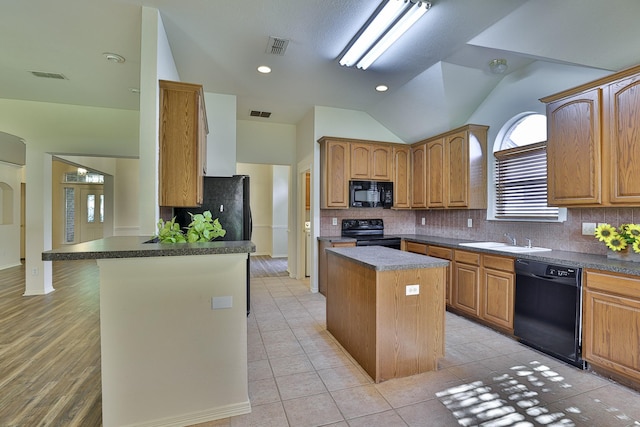 kitchen featuring light tile patterned flooring, lofted ceiling, black appliances, a kitchen island, and kitchen peninsula