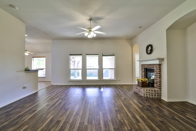 unfurnished living room featuring ceiling fan, dark wood-type flooring, and a brick fireplace