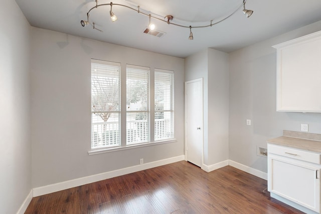 unfurnished dining area featuring rail lighting, dark hardwood / wood-style floors, and a wealth of natural light