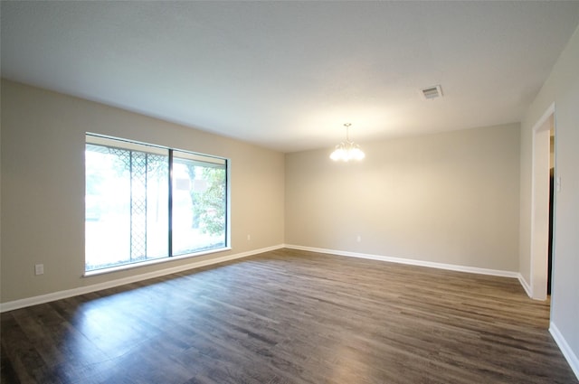 spare room with dark hardwood / wood-style flooring and an inviting chandelier